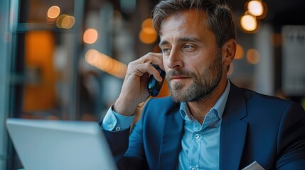 A mature man dressed in a blue suit is using his phone in a stylish and contemporary office environment, indicating a professional and efficient work setting with a warm ambiance.