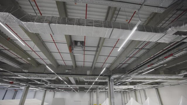 Wide view of technology routes hanged under ceiling. Interior of new industrial building. Rows of led lights, sprinklers and air condition piping.
