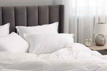 Many soft pillows on bed and bedside table at home