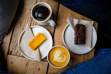 Coffee break. Two mugs of American and latte art on a wooden background. Chocolate brownie and yuzu cake slices. Delicious sweet food and coffees. Flat white, latte. Food and drink.