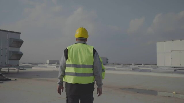 Forwards tracking of male supervisor on construction site. Walking on roof with skylights and air condition units.
