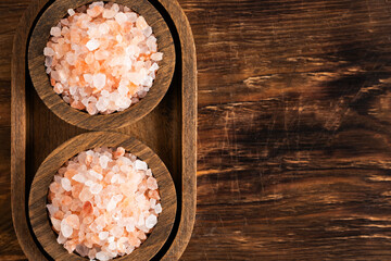 Himalayan salt in wooden bowls on wooden background, top view.