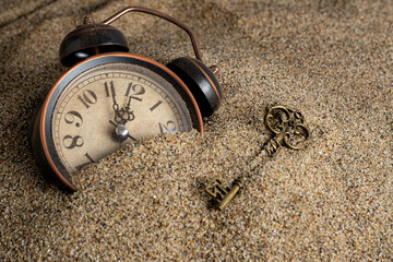 Vintage alarm clock and key in sand. Time management concept.