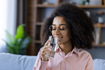 A young woman is seen enjoying a refreshing glass of water at home. She appears relaxed and content, promoting concepts of hydration, health, and wellbeing.