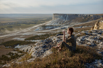Naklejka premium Woman sitting on cliff edge overlooking valley and mountains in travel adventure beauty scene