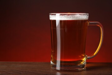 Mug with fresh beer on wooden table against color background, closeup. Space for text