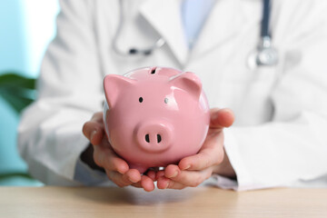 Doctor with piggy bank at wooden table, closeup