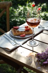 Delicious Belgian waffles with fresh strawberries and wine served on table in garden