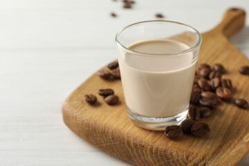 Coffee cream liqueur in glass and beans on white wooden table, closeup. Space for text