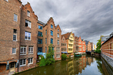 Historic red brick homes and waterfront cafes line the canals and River Leie on an overcast day in the old town medieval center of Ghent, Belgium.
