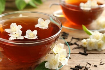 Hot jasmine tea in cups and flowers on wooden table, closeup
