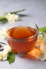 Hot jasmine tea in cup and flowers on light grey table