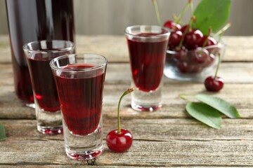 Bottle and shot glasses of delicious cherry liqueur with juicy berries on wooden table, closeup