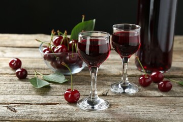 Bottle and glasses of delicious cherry liqueur with juicy berries on wooden table