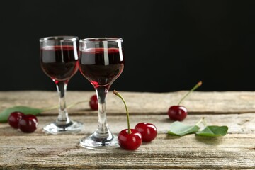 Glasses of delicious cherry liqueur on wooden table against dark background, space for text