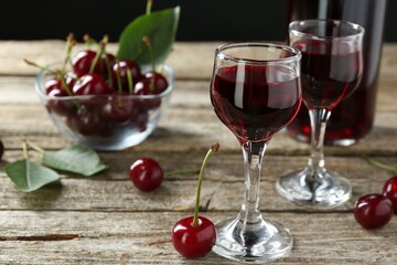 Bottle and glasses of delicious cherry liqueur with juicy berries on wooden table, closeup