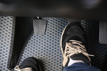 Man in sneakers pushing on pedal of car brake, closeup