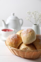 Delicious dough balls with powdered sugar in basket, tea, teapot and gypsophila flowers on white wooden table