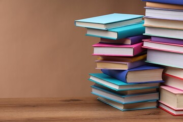 Stacks of colorful books on wooden table against light brown background, space for text