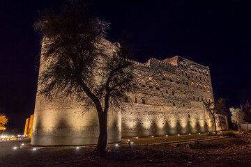 Jabreen citadel fortress stone walls and round bastion tower in night illumination with tree in the...