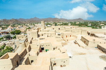 Bahla citadel fortress inner yard buildings and round tower with town in the background, Bahla, Oman
