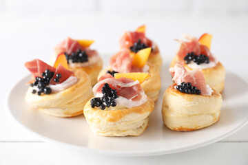 Delicious puff pastry with cream cheese, ham, black caviar and peach on white wooden table