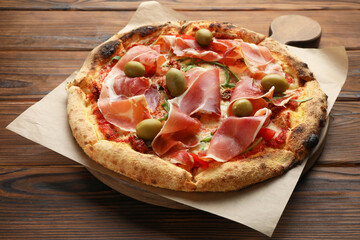 Tasty pizza with cured ham, olives and sun-dried tomato on wooden table