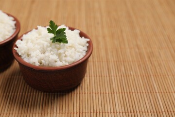 Bowls of delicious boiled rice with parsley on bamboo mat. Space for text