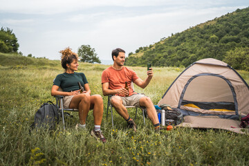 Couple drink beer and boyfriend use mobile phone on camp