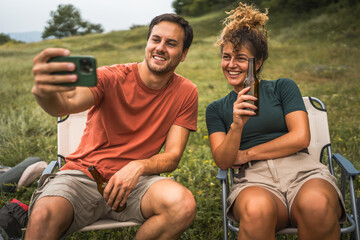 Couple drink beer and take self portrait of them on camp