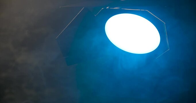 Switching off a spotlight with a blue light on a film set against a backdrop of smoke.