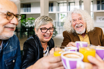 Happy young group of senior people having breakfast together at coffee bar. Elderly lifestyle and friendship concept.