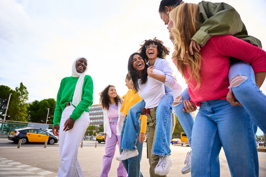 Low angle group of young multi-ethnic only women friends walking fun piggyback sharing happy time of urban female leisure enjoying together in city. Generation z youth empowered girls community people