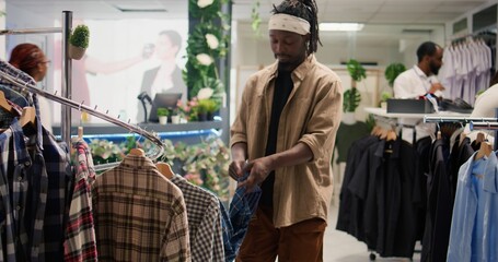 Client browsing through wares in mall clothing store during promotional season, looking to buy clothes to fill his wardrobe. Man taking advantage of sales in fashion boutique, looking at cozy shirts