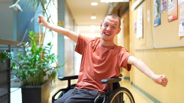 Proud man with disability celebrating in the university sitting on wheelchair and raising arms smiling at camera