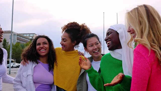 Young multicultural group of women laughing together outdoor. Empowerment concept with united diverse girls from different countries embracing each other while having fun at city street.