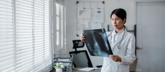 Fototapeta premium Female doctor in white coat carefully examining an X-ray image in a well-lit, modern medical office.