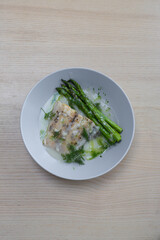 A plate of barramundi and asparagus with veloute sauce.