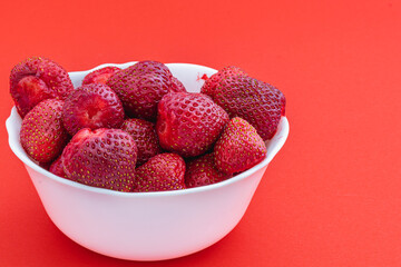 Fresh and ripe strawberries in a white bowl on red background