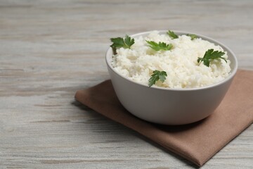 Tasty cooked rice with parsley in bowl on wooden table. Space for text