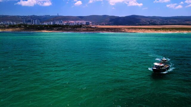 Aerial Backward Panning Shot Of Boats Moving On Wavy Sea By City Near Mount Carmel Mountain Range - Haifa, Israel