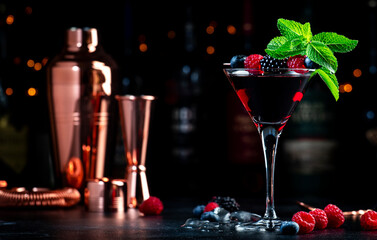 Summer alcoholic cocktail with berries, rum, juice, mint and ice, black background with bottles