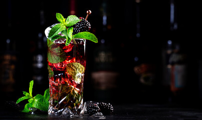 Summer blackberry low alcohol cocktail with rum, tonic, mint and ice, black background with bottles