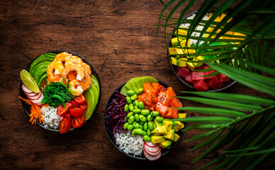 Balanced diet poke bowls with tuna, salmon, shrimp, vegetables, legumes, avocado and rice, wood table background, top view