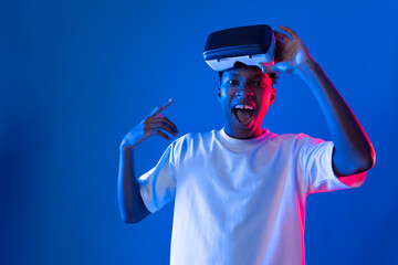 Surprised young African American looking through VR holding interesting object hologram on pink...