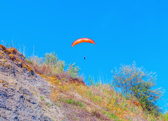 Paragliding over a hill. Person is flying a parachute on a hill
