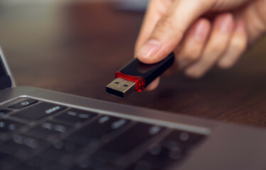 Hand holding usb flash drive with connecting to laptop at wooden table