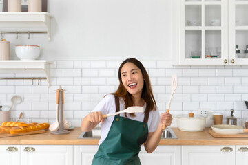 Young Asian woman dancing in the kitchen. The joy of a beautiful woman relaxing in her free time during the weekend in the house