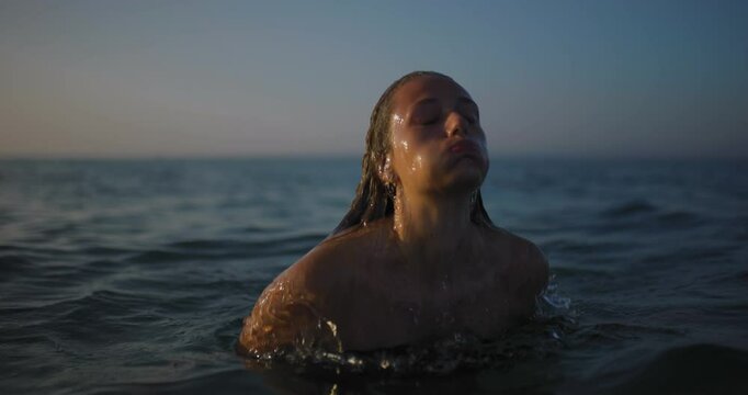 Serene woman emerging from the sea at sunset, peaceful water relaxation