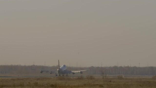 A huge four-engine wide-body aircraft with an unrecognizable livery takes off, rear view. Footage of an airliner taking off